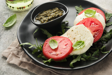 Caprese salad. Italian caprese salad with sliced tomatoes, mozzarella cheese, arugula, basil, olive oil in black plate over old concrete gray background. Delicious Italian food. Top view.