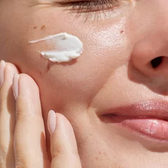 Hydration. Cream smear. Beauty close up portrait of young woman with a healthy glowing skin is applying a skincare product. © Beauty Agent Studio