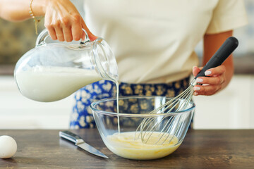 Close up hand adds milk to the dough for pancake. Ingredients for focaccia, pie, pizza, ravioli, pasta. bakery, cookbook, cooking blog.