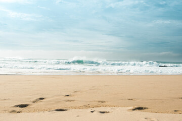 Fototapeta na wymiar View of sandy beach with waves crashing. Tranquil scene of empty beach and cloudy sky