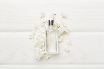 Face serum with flowers on wooden background, top view