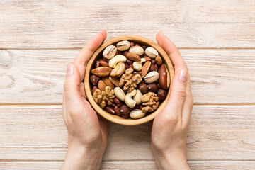 Woman hands holding a wooden bowl with mixed nuts Walnut, pistachios, almonds, hazelnuts and...