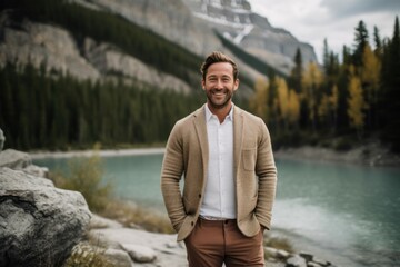 Handsome man standing in front of a mountain lake and smiling