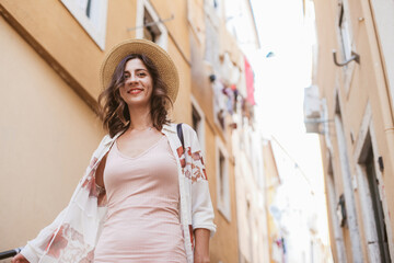 Pretty woman in a straw hat and a pink summer dress walking on sunny streets of Lisbon