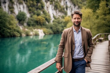 Naklejka premium Handsome bearded man in a beige jacket on the background of the emerald water of the lake