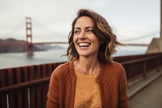 Lifestyle portrait photography of a grinning woman in her 30s that is wearing a chic cardigan at the Golden Gate Bridge in San Francisco USA . Generative AI