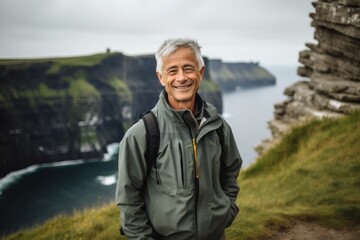 Naklejka premium Portrait of a smiling senior man standing in front of the Cliffs of Moher in Ireland