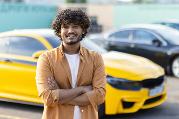 Portrait of a young smiling hispanic man against the background of a sports yellow car. He is...