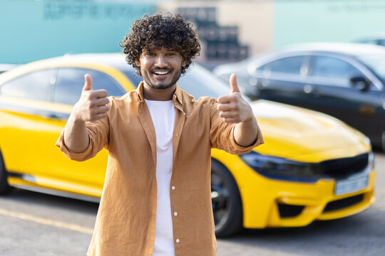 Young successful hindu programmer entrepreneur outside office building smiling and looking at camera man showing thumbs up joyfully near his new car, business owner satisfied with achievement results - Powered by Adobe