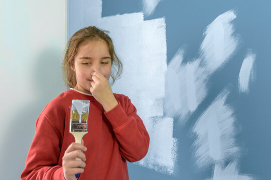 Girl covers her nose from the smell of paint while painting the walls