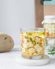 Marinated feta cheese cubes in olive oil in a glass jar. Cheese cubes marinating in olive oil, feta cheese in olive oil with rosemary with dried pepper and tomatoes