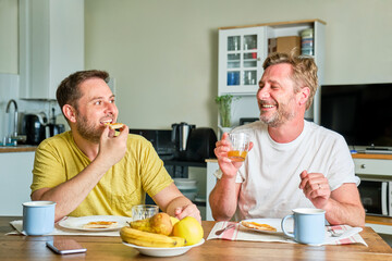 gay couple of two mature guys at home having breakfast toast with fruit juice