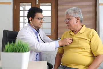young Indian doctor sitting with a senior patient in the room of a nursing home. An elderly patient having a detailed conversation with personal doctor during their visit. Examining the elderly man 