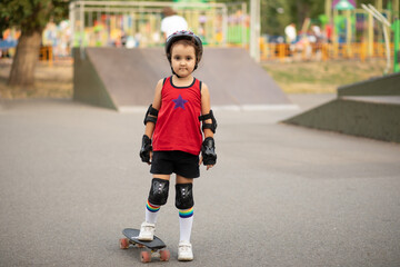 Cute kid girl child with skateboard in a hands standing in a skatepark and smiling. Child performs tricks. Summer sport activity concept.