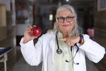 Happy Indian female doctor holding an apple in her hand and portraying message to have a better...