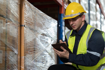 Male warehouse worker wearing uniform checks stock inventory in warehouse. Male worker holding clipboard and checking barcodes on boxes on shelf pallet in storage warehouse
