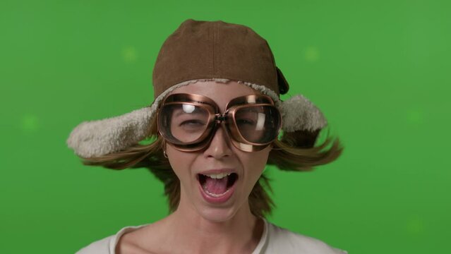 Close-up of a girl's face in a retro pilot's hat blown by a strong wind on Green screen background, chroma key.
