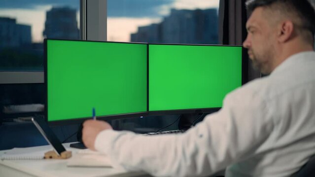 Man Uses Desktop Computer With Two Green Screen Mock Ups Working at Home. Close Up of Monitors With Green Screen On Desktop