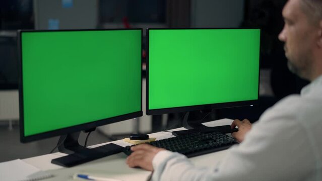 Man Uses Desktop Computer With Two Green Screen Mock Ups Working at Home. Close Up of Monitors With Green Screen On Desktop
