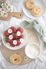A plate of strawberries is decorated with white daisies. Berries with vitamins and a cup of aromatic coffee