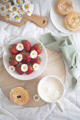 A plate of strawberries is decorated with white daisies. Berries with vitamins and a cup of aromatic coffee