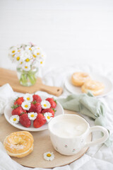 A plate of strawberries is decorated with white daisies. Berries with vitamins and a cup of aromatic coffee