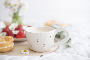 A plate of strawberries is decorated with white daisies. Berries with vitamins and a cup of aromatic coffee