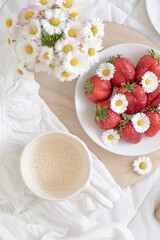 A plate of strawberries is decorated with white daisies. Berries with vitamins and a cup of aromatic coffee