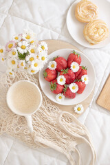 A plate of strawberries is decorated with white daisies. Berries with vitamins and a cup of aromatic coffee