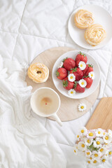 A plate of strawberries is decorated with white daisies. Berries with vitamins and a cup of aromatic coffee