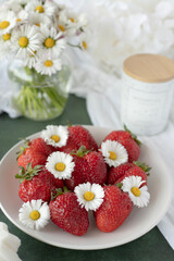 Fototapeta na wymiar A plate of strawberries is decorated with white daisies. Berries with vitamins