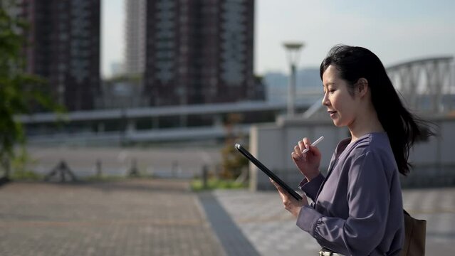 タブレットに書きこみながら歩くビジネスウーマンのサイドショット