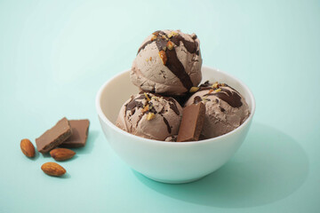 Chocolate ice cream decorated with nuts and chocolate icing, in a white bowl, blue background....