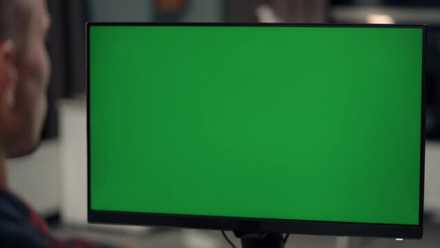 Young Man Working At Computer With Green Mock Up Screen in Home. Close Up Desktop Computer Monitor with Mock Up Green Screen Chroma Key Display