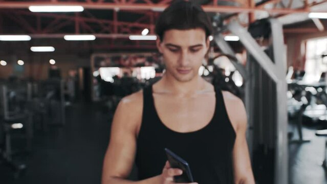 Portrait of confident bodybuilder looking phone screen at gym and showing green screen. Close-up serious fitness man using mobile phone in sport club