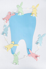 Easter dentistry. Blue tooth and garland of rabbits on a white background, top view