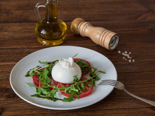 Burrata cheese with tomatoes, arugula and pesto sauce on a white plate.