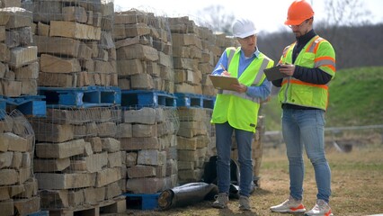 Closeup of woman project engineer reviewing use of stone with job foreman on a construction site.