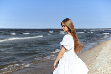 Fototapeta na wymiar Happy, beautiful woman on the ocean beach standing in a white summer dress. Portrait.