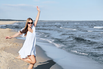 Happy blonde woman having fun on the ocean beach in a white dress and sunglasses.