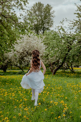 Fototapeta premium Girl in white dress running through a blossoming apple orchard