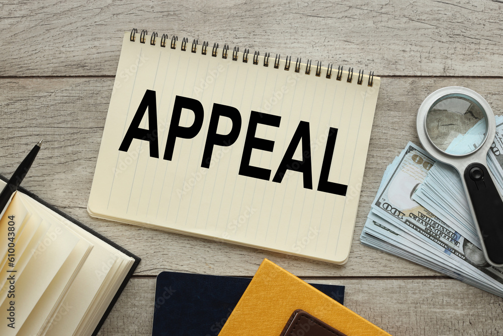 Poster appeal text on a page of a notebook near a yellow notebook with a magnifying glass and banknotes of 