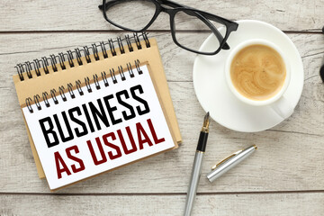 BAU - Business as Usual acronym, business concept . a wooden light background a page with text with a cup of coffee and glasses