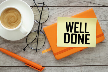 Well done text on a yellow note and a table with an orange notepad.