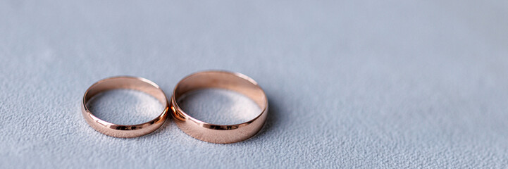 Two gold wedding rings lie on a white surface. The concept of wedding accessories, preparation for the wedding ceremony. Banner for website header design with copy space.