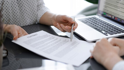 Obraz premium Business people sitting and discussing contract in office, closeup. Partners or lawyers working together at meeting before signing papers. Teamwork and partnership.