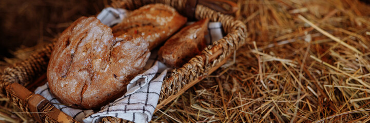 Rustic still life: a wicker tray, a loaf of homemade bread on a tablecloth on a roll of hay. Traditional farm lunch. Photo of healthy food.