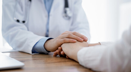 Doctor and patient sitting at the wooden table in clinic. Female physician's hands reassuring woman. Medicine concept.