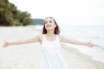 Fototapeta na wymiar Happy smiling woman in free happiness bliss on ocean beach standing with open hands. Portrait of a multicultural female model in white summer dress enjoying nature during travel holidays vacation outd