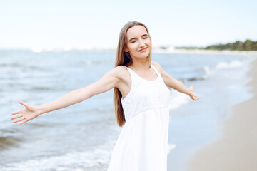 Fototapeta na wymiar Happy smiling woman in free happiness bliss on ocean beach standing with open hands. Portrait of a multicultural female model in white summer dress enjoying nature during travel holidays vacation outd
